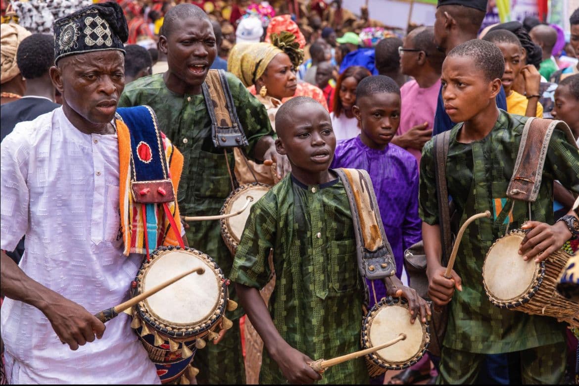 Yoruba drummers in traditional attire playing talking drums at a celebration